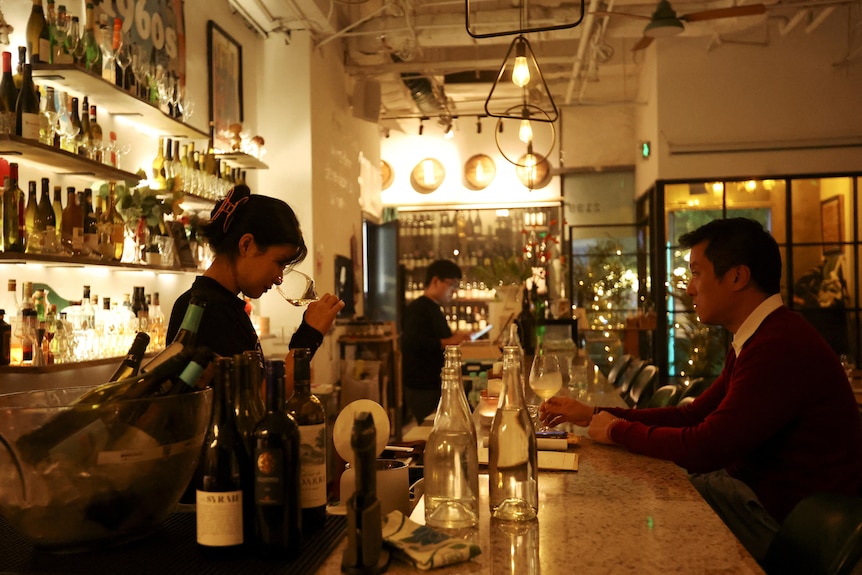 A woman works in a wine bar as a man sits at the bar.