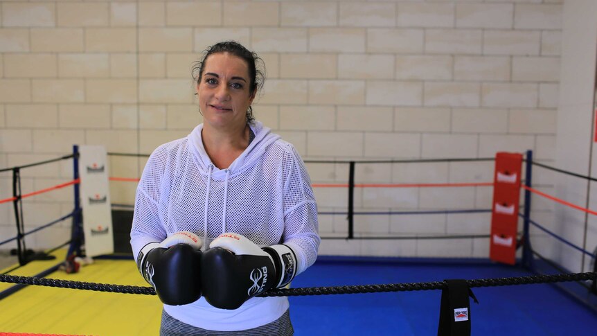 A woman stands in a boxing ring wearing boxing gloves