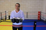 A woman stands in a boxing ring wearing boxing gloves