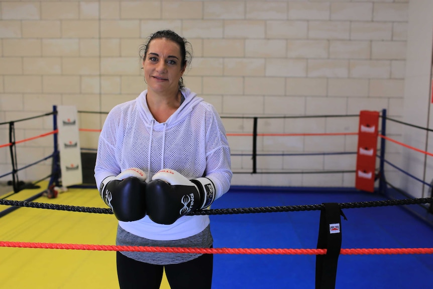 A woman stands in a boxing ring wearing boxing gloves