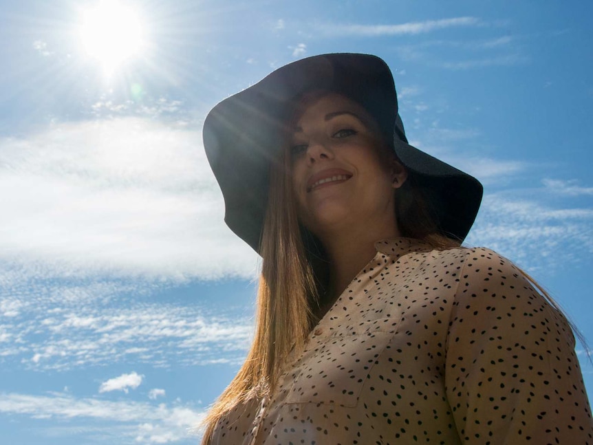 A woman wears a hat with the sun in the background.