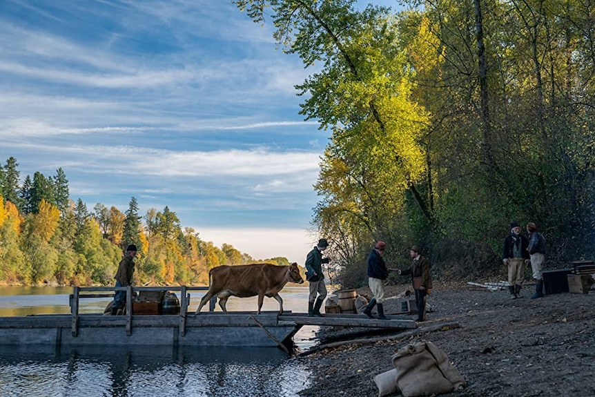 Film still of men including John Magaro as Cookie and Orion Lee as King-Lu leading a cow over a bridge from First Cow