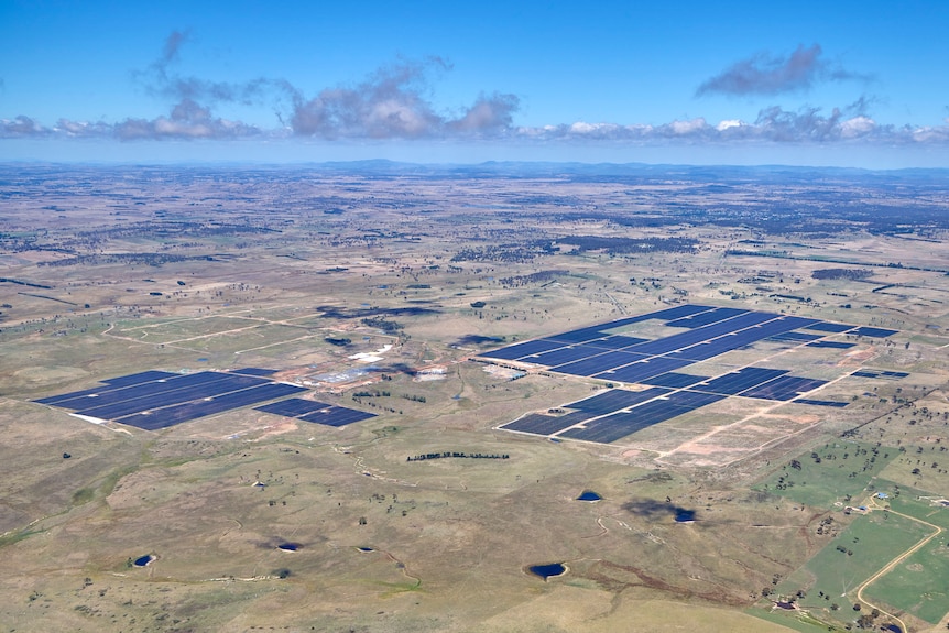 An aerial view of cleared farmland with dark patches of solar panels
