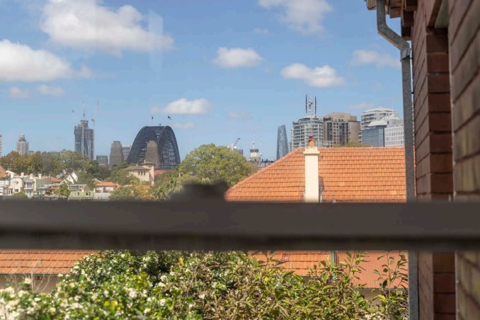 The top of the Sydney harbour bridge and tall buildings can be seen out the window of an apartment beyond the roofs of homes
