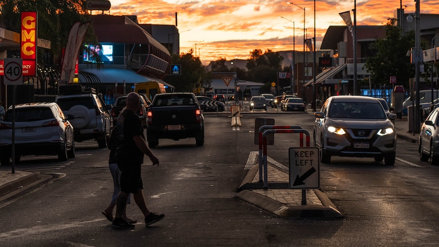 People and cars on a busy street in the Alice Springs CBD as the sun sets on the horizon. 