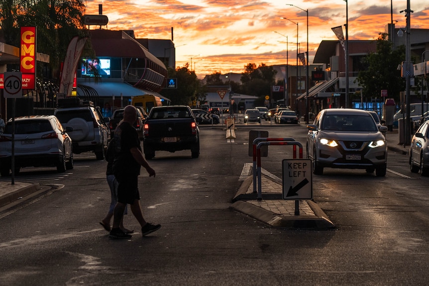 People and cars on a busy street in the Alice Springs CBD as the sun sets below the horizon. 