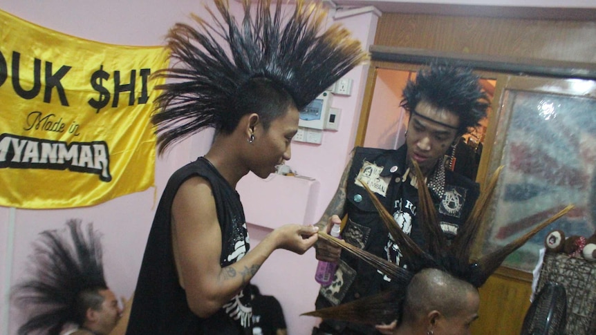A man with a mohawk straightens the hair of another punk man.
