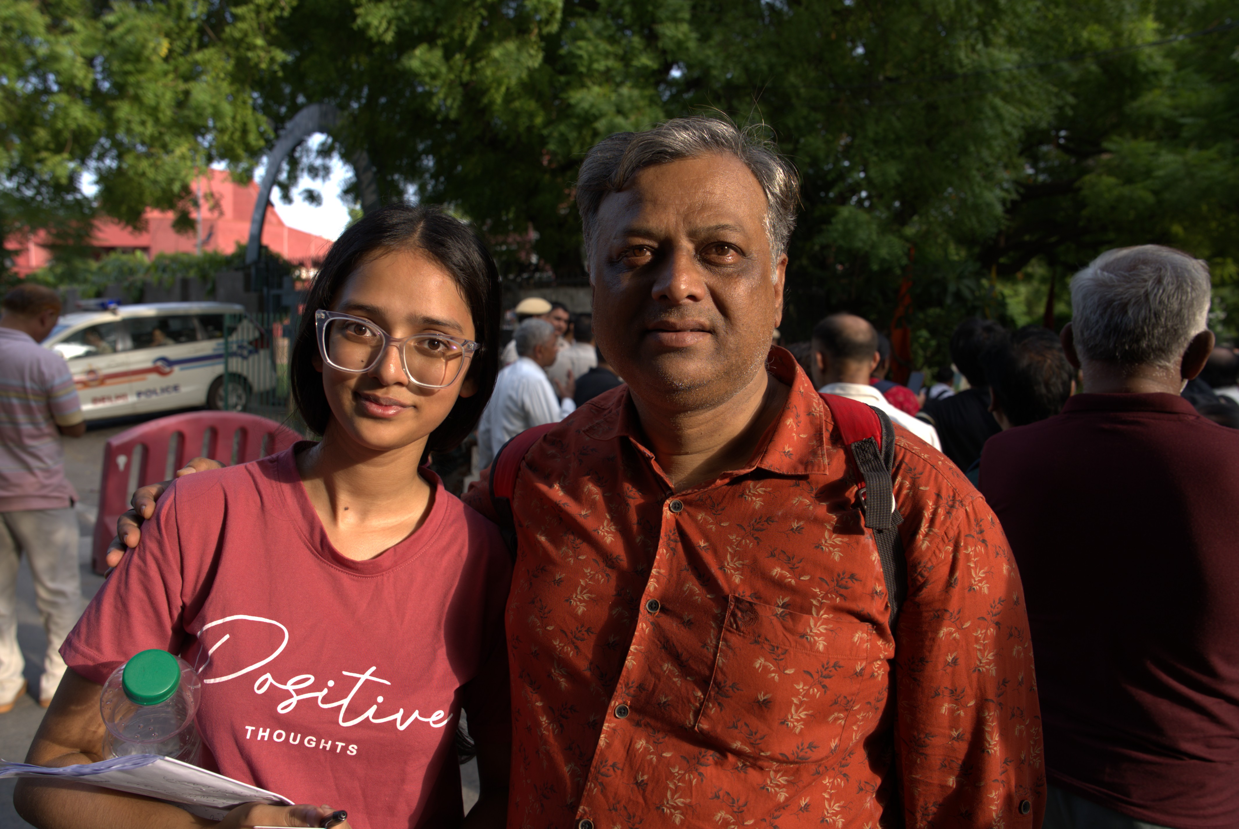 An Indian man and his daughter smliing in a portrait taken outdoors.