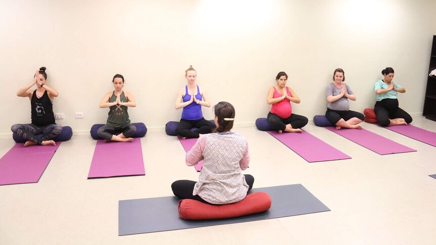 A group of pregnant women sitting on yoga mats in a cross-legged pose.