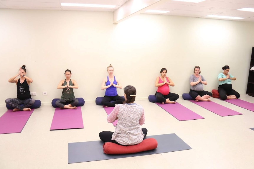 A group of pregnant women sitting on yoga mats in a cross-legged pose.