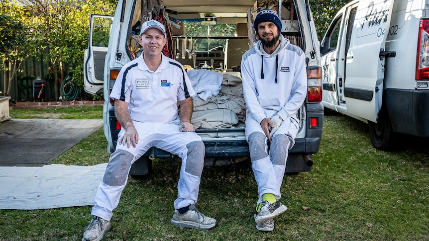 Two men sitting in the back of a painter's van.