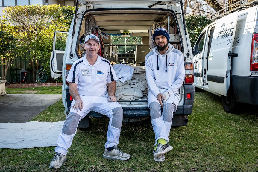 Two men sitting in the back of a painter's van.