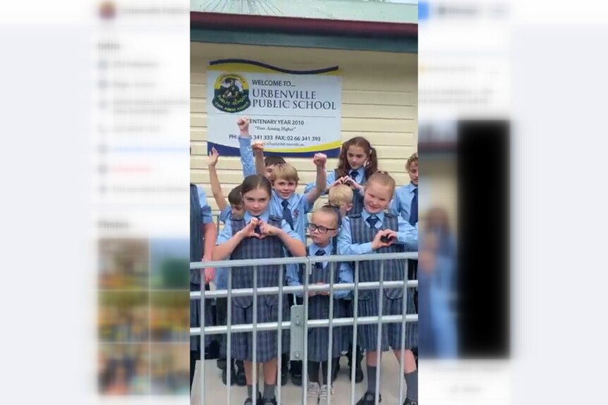 A screen shot of a Facebook video with school children in front of a school sign