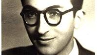 A black and white image shows a man wearing round thick rimmed glasses.