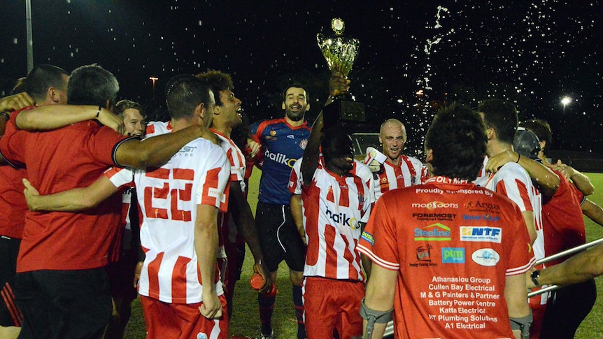 Darwin Olympic Sporting club soccer team celebrating a win on pitch with a trophy