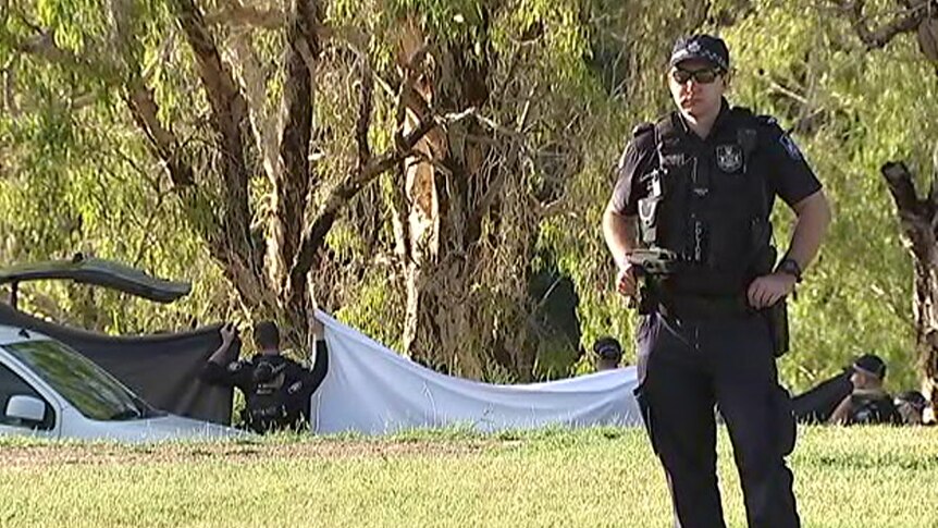 Police officers hold up sheets at the bank of the Ross River in Townsville.