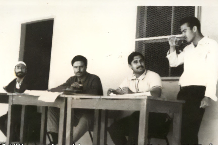 Old black and white photo of four men sitting at a table.