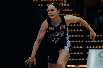 A brunette woman with slicked back hair runs on a basketball court and bounces a ball. 