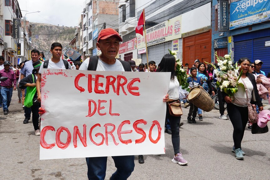 A man holds a sign saying "Cierre Del Congreso" in red ink amid a funeral procession. 