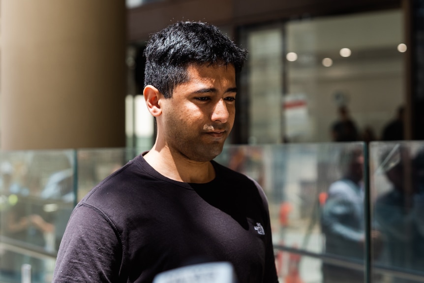 A head and shoulders shot of a man with short hair looking downwards while walking outside.