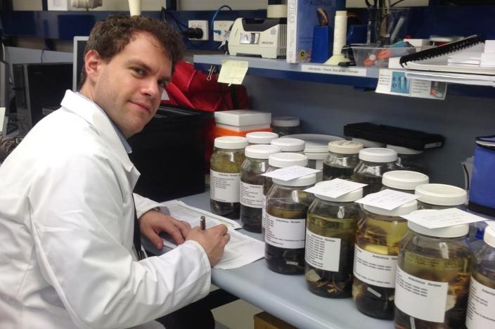 Photo of a white man in a lab coat with specimen jars