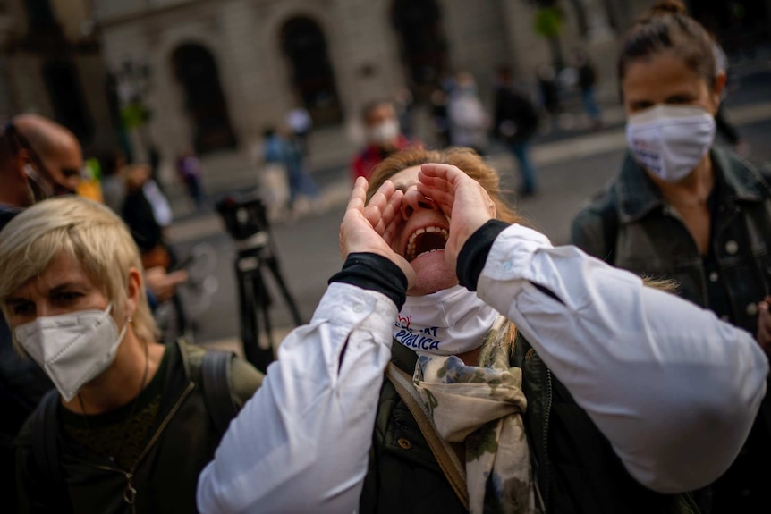 A woman frames her mouth with her hands as she screams while other people wearing masks watch on.