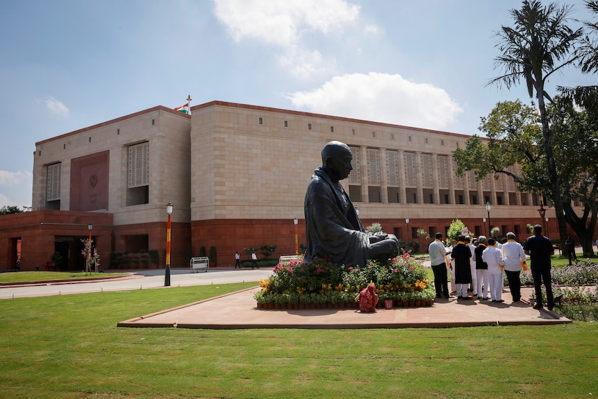 A statue of Mahatma Gandhi is pictured next to India's new parliament building under a clear blue daylight sky.