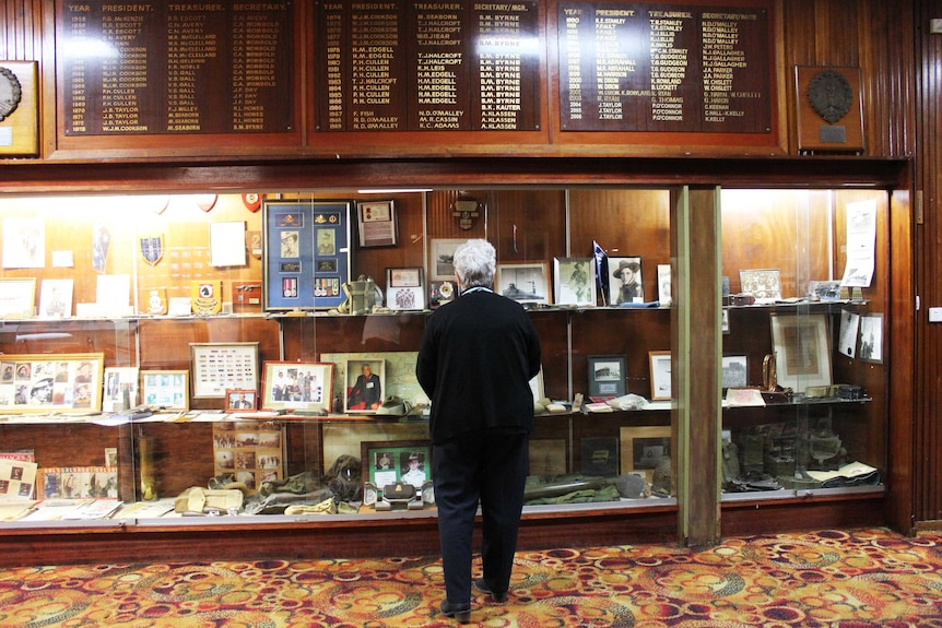 A woman stands in front of war memorabilia, including medals, photographs, plaques, at an RSL
