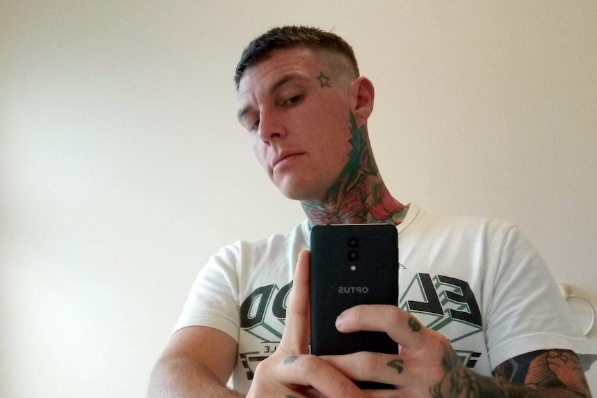 A man with lots of tattoos takes a selfie in the mirror with a mobile phone.