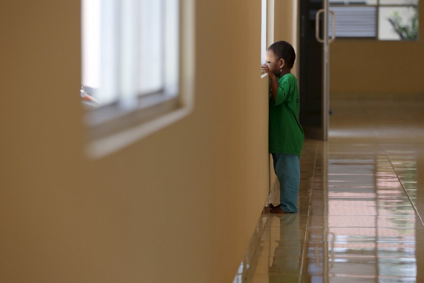 A child peers out the window of a building with their hands on the window ledge.