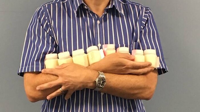 Man standing holding very small bottles of milk