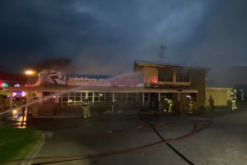 Firefighters using a hose to put out a fire in a shop, at night.