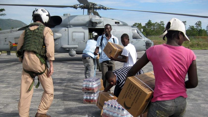 Local Haitians help unload bottled water from a US Navy Helicopter