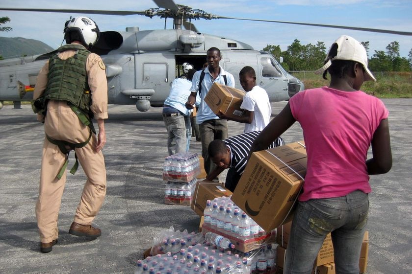 Local Haitians help unload bottled water from a US Navy Helicopter