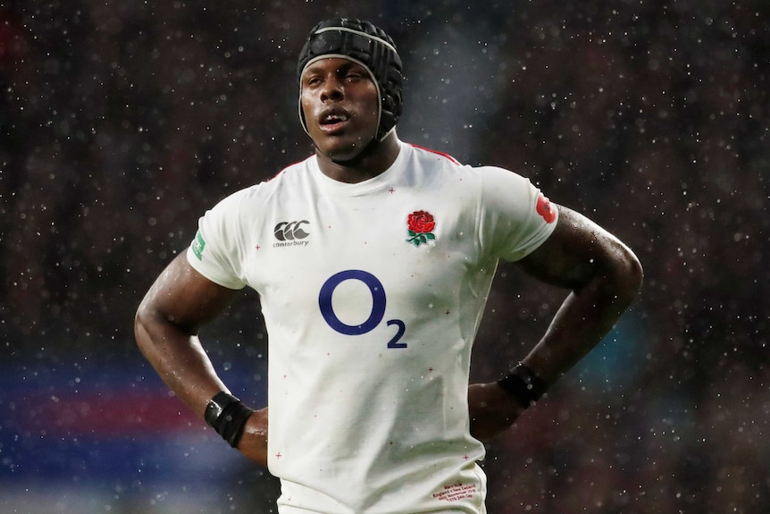 A male rugby union player wearing head gear stands with his hands on his hips.