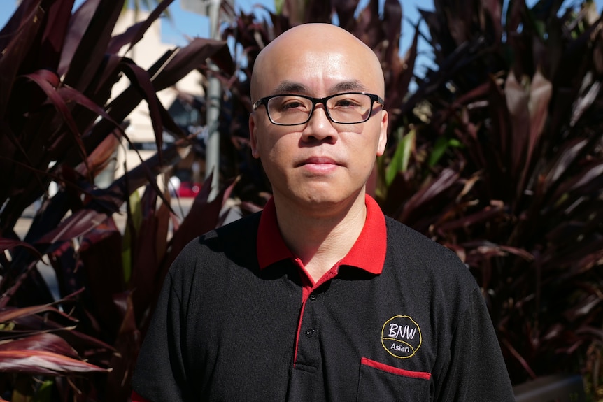 Eric Yip wearing glasses, black polo shirt that says BNW Asian, looking at the camera straight-faced.