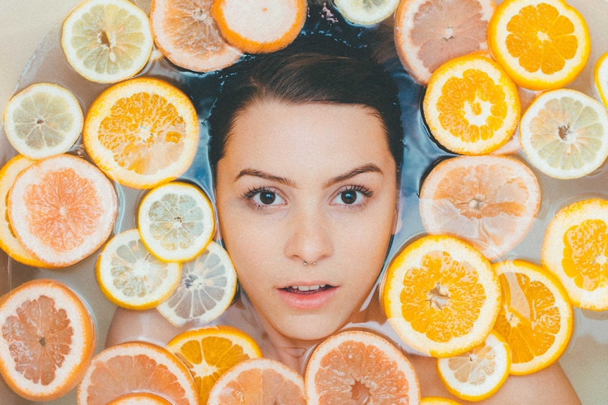 Female face surrounded by floating fruits in bath.