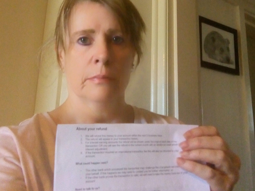 A woman holds up a piece of paper and looks upset.