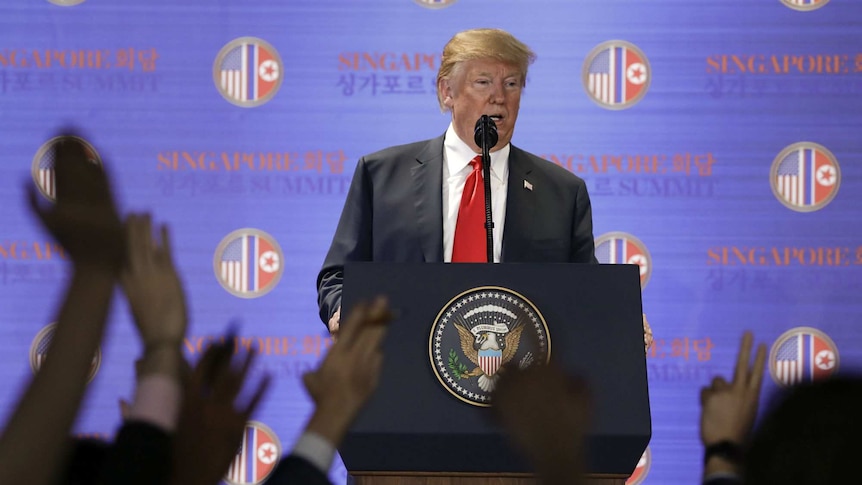 US President Donald Trump taking questions from reporters with raised hands.