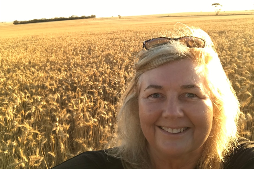 A blonde lady stands in from of a golden wheat crop