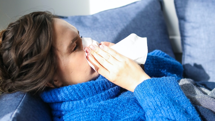 Woman in blue jumper blows her nose.