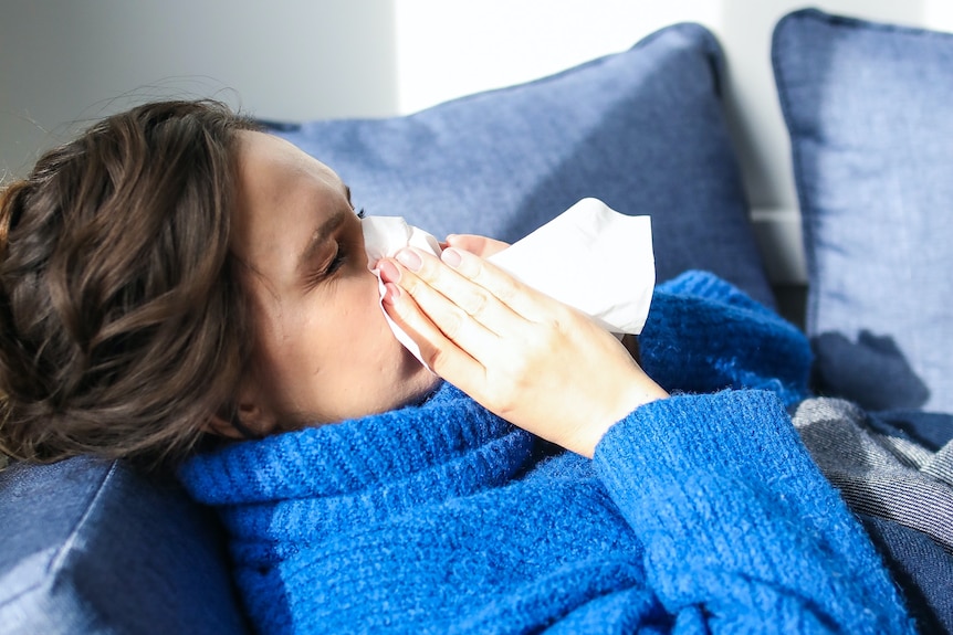 Woman in blue jumper blows her nose.