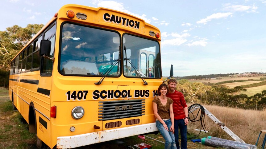 Tobias Bockholt and Marisa Schlichthorst stand with the big yellow ex-school bus they are renovating