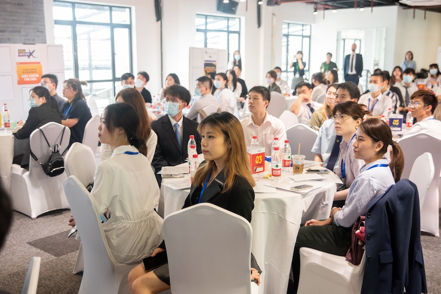 A room full of university-aged people in a conference-style room in an Asian city