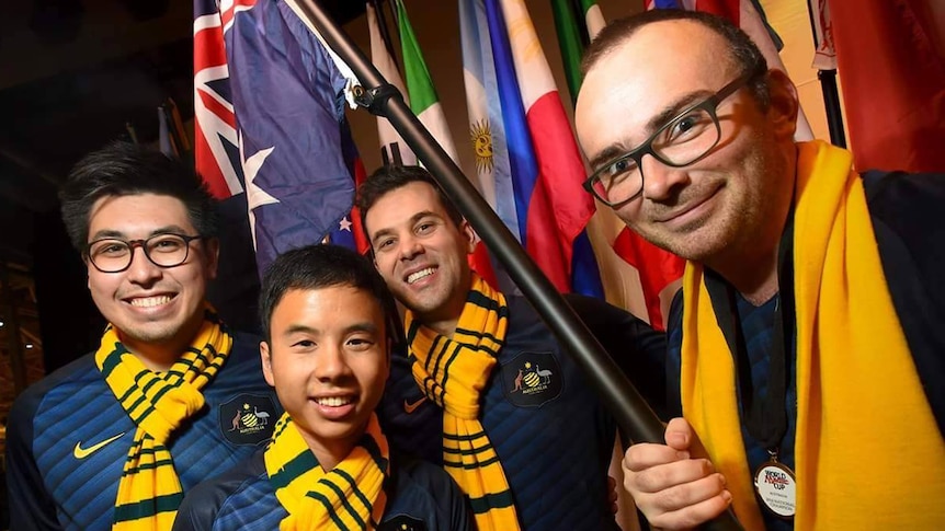 Four men wearing matching uniforms and waving a flag.