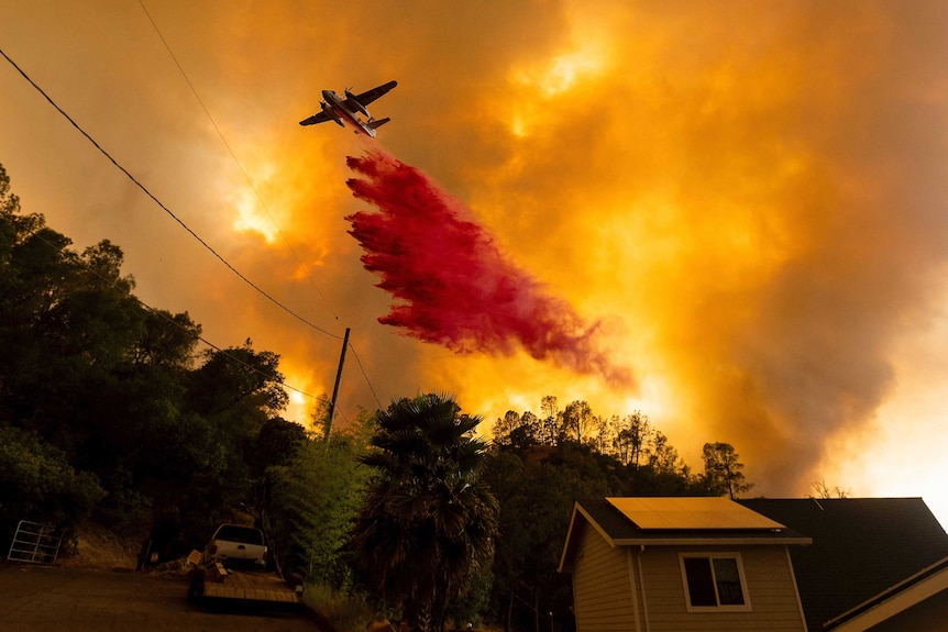 An air tanker drops red retardant on orange flames over the California wildfires.