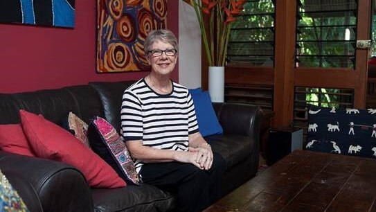 Clare Martin sits on a couch in a black and white striped t-shirt and glasses.