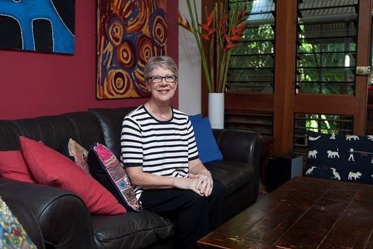 Clare Martin sits on a couch in a black and white striped t-shirt and glasses.