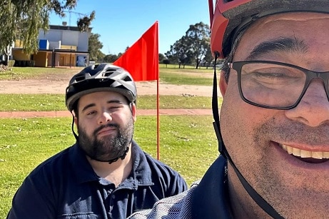 Close up of faces of a man and his adult son wearing bike helmets on a sunny day.