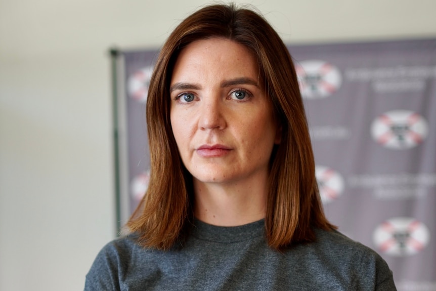 A woman with brown hair wearing a grey top with the letters AEA on it